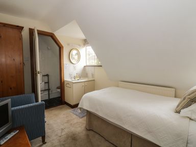A bedroom with a bed a chair a wardrobe a sink and a bathroom at The Lodge off High Street in Hadleigh