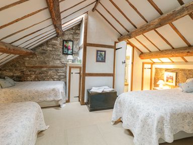 A bedroom with two beds quilted bedspreads wooden beams and stone walls at Lower Dolgenau The Cottage in Llawryglyn near Llanidloes