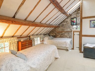 A bedroom with two single beds wooden beams stone wall and a chest at Lower Dolgenau- The Cottage in Llawryglyn near Llanidloes