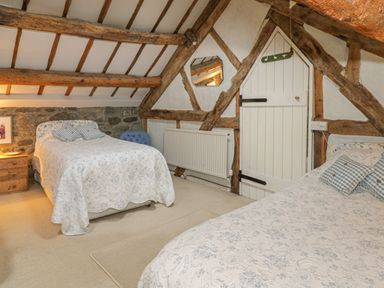 A bedroom with two beds wooden beams and a small door at Lower Dolgenau The Cottage in Llawryglyn near Llanidloes