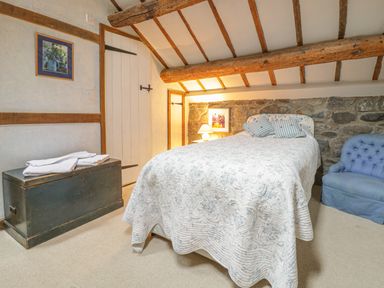 A bedroom with a bed a wooden chest a blue armchair and exposed beams at Lower Dolgenau The Cottage in Llawryglyn near Llanidloes