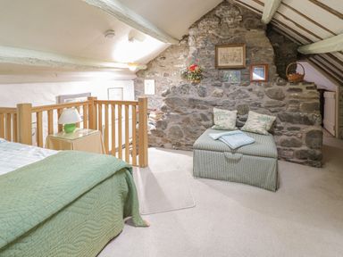 A bedroom with a green bedspread wooden railing lamp and a stone wall with framed pictures at Lower Dolgenau The Cottage in Llawryglyn near Llanidloes