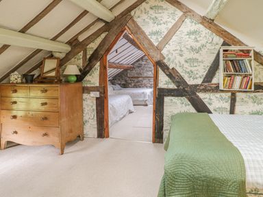 A bedroom with a green bedspread a wooden chest of drawers a small bookshelf and a view into another room with two beds at Lower Dolgenau- The Cottage in Llawryglyn near Llanidloes