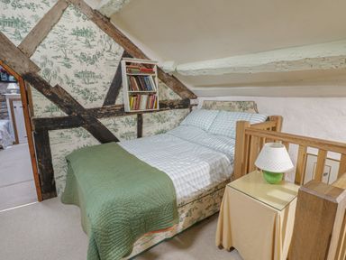 A small bedroom with a double bed with patterned bed frame and green blanket and a bedside table with a lamp at Lower Dolgenau The Cottage in Llawryglyn near Llanidloes