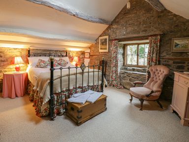 A bedroom with a metal bed frame floral curtains and a wooden chest at Lower Dolgenau The Cottage in Llawryglyn near Llanidloes