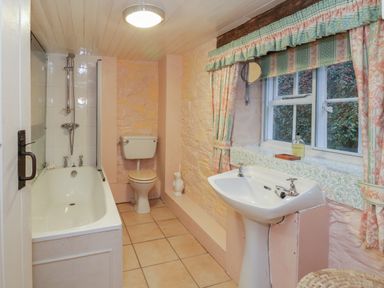 A bathroom with a bathtub toilet sink and a window with curtains at Lower Dolgenau- The Cottage in Llawryglyn near Llanidloes