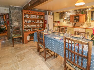 A kitchen with a dining table set with plates and glasses next to a wooden cupboard with crockery at Lower Dolgenau The Cottage in Llawryglyn near Llanidloes