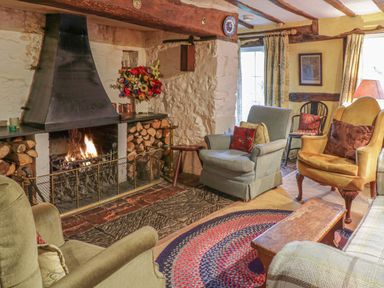 A living room with a lit fireplace wooden logs on each side different armchairs and a round rug at Lower Dolgenau The Cottage in Llawryglyn near Llanidloes