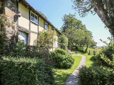 A garden pathway beside a house with windows and bushes at Lower Dolgenau The Cottage in Llawryglyn near Llanidloes
