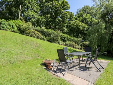 A garden patio with a table and four chairs surrounded by grass and trees at Lower Dolgenau- The Cottage in Llawryglyn near Llanidloes