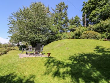 A grassy garden with a patio table and chairs under a tree at Lower Dolgenau The Cottage in Llawryglyn near Llanidloes