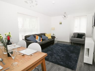 A living room with a black sofa and a gray armchair near windows with blinds at 11 Camden Building in Kendal