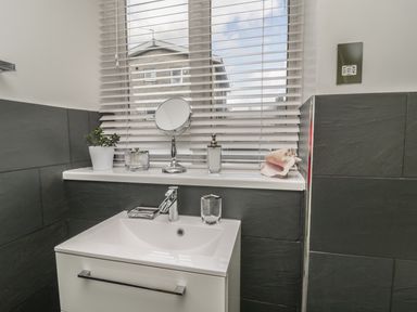 A bathroom sink with a faucet toothbrush holder and soap dispenser in front of a window with blinds at 11 Camden Building in Kendal