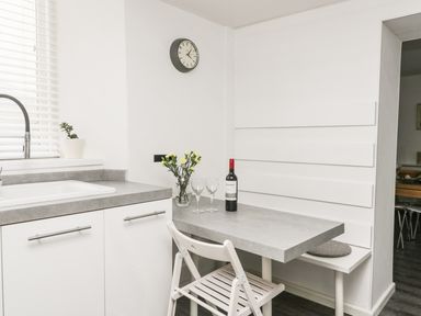 A kitchen corner with a gray countertop a sink a small table with a bottle of wine two glasses and yellow flowers at 11 Camden Building in Kendal