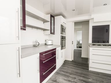 A kitchen with white and purple cabinets a countertop with a toaster and coffee press built in microwave and oven and a gas stove at 11 Camden Building in Kendal