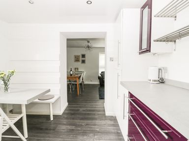 A kitchen with white and purple cabinets a white kettle and a small dining area with flowers on the table at 11 Camden Building in Kendal