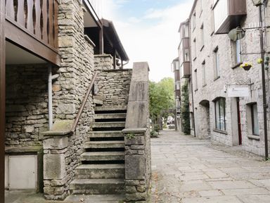 Stone steps with a handrail next to a stone building on a cobblestone street with trees and buildings at 11 Camden Building in Kendal