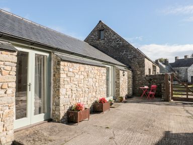An outdoor stone patio area with flower pots and a red table and chairs set at Poppy Cottage in Llantwit Major