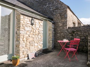 An outdoor patio with stone walls a pink table and two pink chairs at Poppy Cottage in Llantwit Major