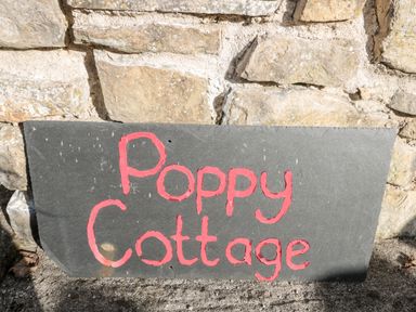 A stone wall with a black slate sign painted with red letters saying Poppy Cottage at Poppy Cottage in Llantwit Major