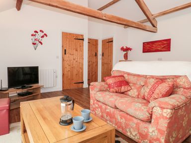 A living room with a patterned sofa coffee table tv and wooden doors at Poppy Cottage in Llantwit Major