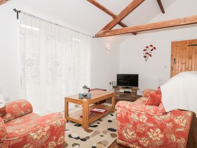 A living room with floral armchairs a wooden coffee table and a television at Poppy Cottage in Llantwit Major