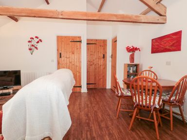 A dining area with wooden table and chairs and wooden doors in a room with exposed wooden beams at Poppy Cottage in Llantwit Major