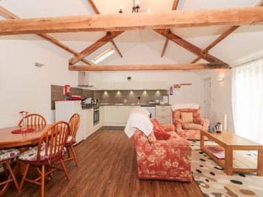 An open kitchen and living area with wooden dining chairs and table floral armchairs wooden coffee table and exposed ceiling beams at Poppy Cottage in Llantwit Major