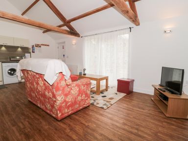 A living room with a floral sofa a wooden coffee table a TV on a stand and kitchen appliances visible at Poppy Cottage in Llantwit Major
