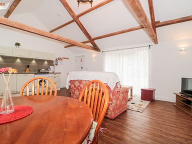 An open living room and kitchen with wooden beams a dining table chairs a sofa and a television at Poppy Cottage in Llantwit Major
