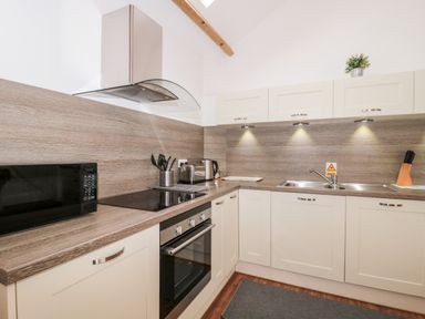 A kitchen with white cabinets a microwave stove oven sink and utensils at Poppy Cottage in Llantwit Major