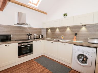 A kitchen with white cabinets a washing machine an oven a microwave and a sink at Poppy Cottage in Llantwit Major