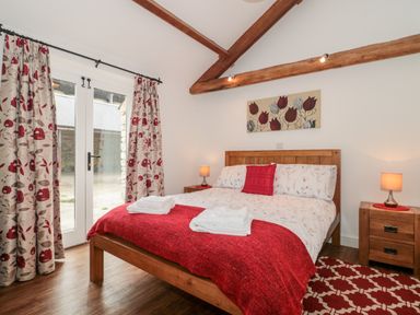 A bedroom with a wooden bed red and floral bedding wooden bedside tables lamps and floral curtains at Poppy Cottage in Llantwit Major