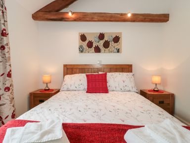 A bedroom with a double bed floral bedding and red accents wooden bedside tables with lamps and wall art above the bed at Poppy Cottage in Llantwit Major