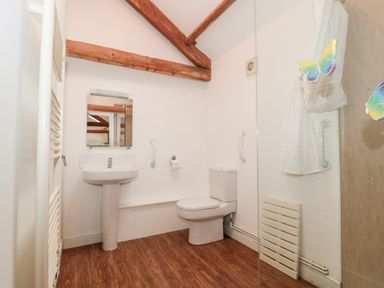 A bathroom with a pedestal sink a toilet wooden beams on the ceiling and wooden floor at Poppy Cottage in Llantwit Major