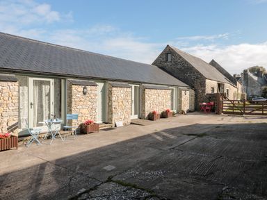 An outdoor area with stone buildings blue and red garden chairs and tables and flower planters at Poppy Cottage in Llantwit Major