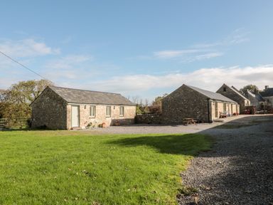 Stone buildings with gravel paths and green grass under a blue sky at Poppy Cottage in Llantwit Major