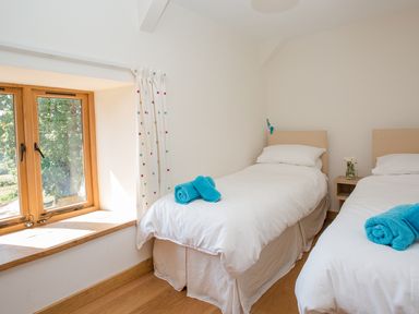 A bedroom with two single beds white bedding blue towels on beds window with wooden frame and white curtains with colored dots at Salters Black Dog near Crediton