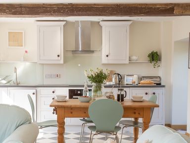 A kitchen with a wooden dining table and green chairs with flowers and breakfast items at Salters Black Dog near Crediton