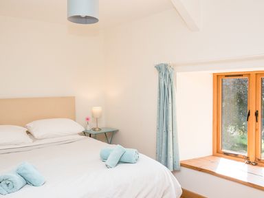 A bedroom with a bed with blue towels and a side table lamp near a window with blue curtains at Salters in Black Dog near Crediton