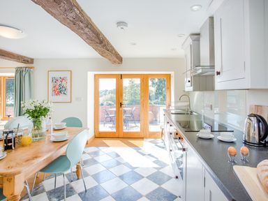 A kitchen with a wooden dining table and chairs next to double glass doors opening to a patio at Salters in Black Dog near Crediton