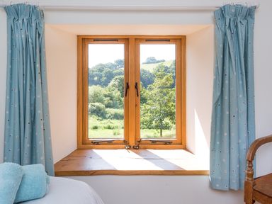 A bedroom window with blue curtains and a wooden chair at Salters in Black Dog near Crediton