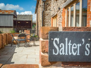 An outdoor patio with a table and chairs next to a brick building and farm structures at Salters in Black Dog near Crediton