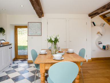 A dining area with a wooden table set with bowls and flowers and light blue chairs at Salters in Black Dog near Crediton