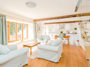 A living room and kitchen with white armchairs a wooden table and cabinets at Salters in Black Dog near Crediton