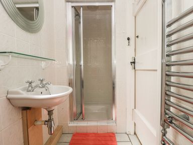 A small bathroom with a sink mirror shower enclosure red bath mat and heated towel rail at Bolitho's Retreat Helford