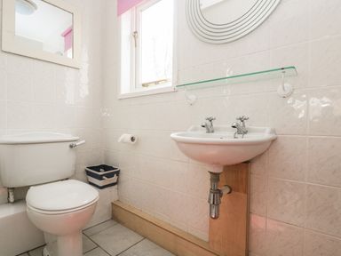 A bathroom with a toilet a sink a mirror a window and a small storage basket at Bolitho's Retreat in Helford