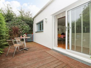 A wooden deck with two chairs and a small table with mugs outside a white house with sliding glass doors at Bolitho's Retreat in Helford