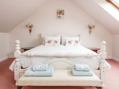 A bedroom with a white bed and floral pillows two wooden side tables and folded towels on a bench at Bolitho's Retreat in Helford