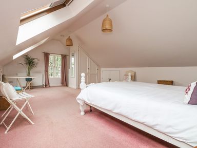 A bedroom with a white bed a folding chair a small round table a plant and skylight windows at Bolitho's Retreat in Helford